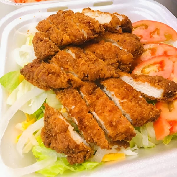 Crispy fried chicken pieces, sliced tomatoes, and shredded lettuce in a white takeout container from Mama Noi's.