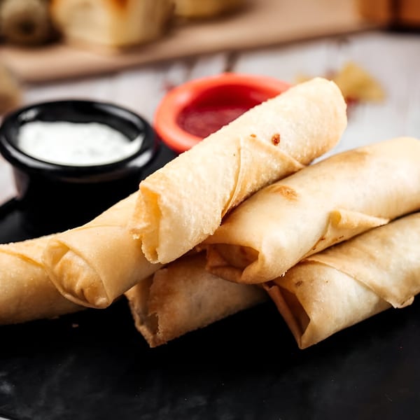Crispy golden spring rolls on a black plate with red and white dipping sauces.