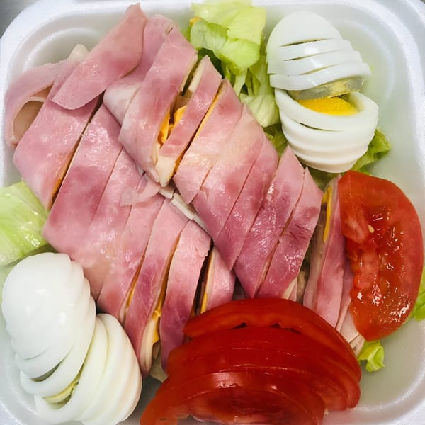 Close-up of a chef salad with ham and cheese rolls, sliced hard-boiled eggs, lettuce, and tomatoes.