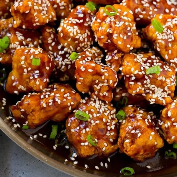 Close-up of Mama Noi's Asian-fusion sesame chicken, glistening with sauce and garnished with green onions.