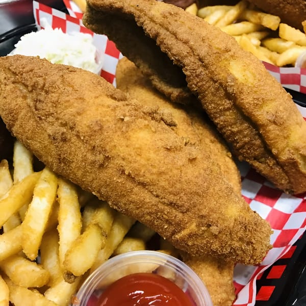 Crispy fried fish fillets with golden french fries, coleslaw, and ketchup in a red and white checkered basket.