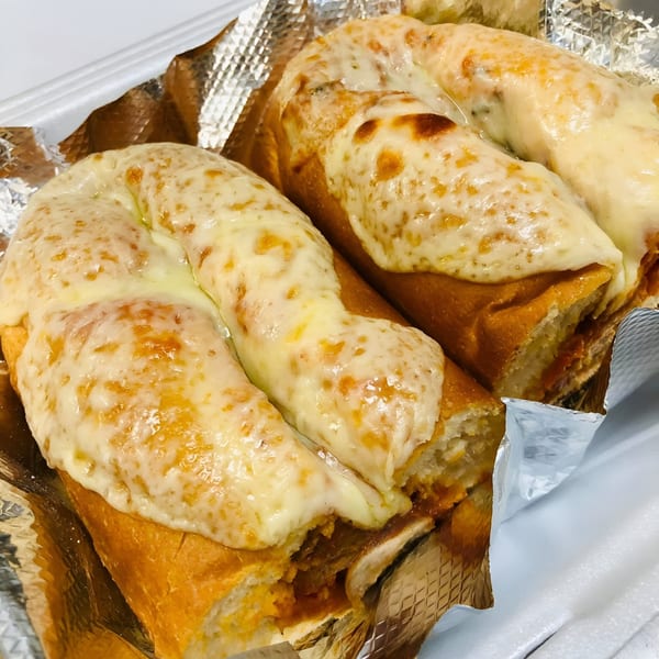 Two cheesy baked subs with golden-brown crusts, filled with a savory mixture, served in foil.