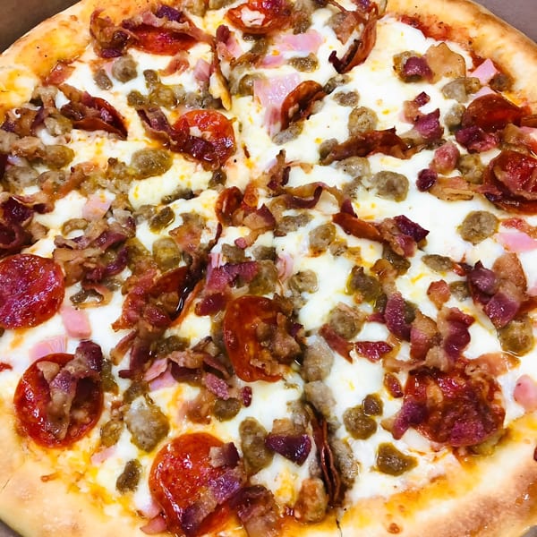A close-up of a Mama Noi's pizza, loaded with pepperoni, sausage, bacon, and ham.