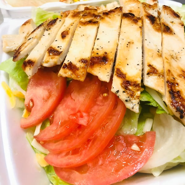 Grilled chicken strips with char marks, sliced tomatoes, and lettuce in a white takeout container.